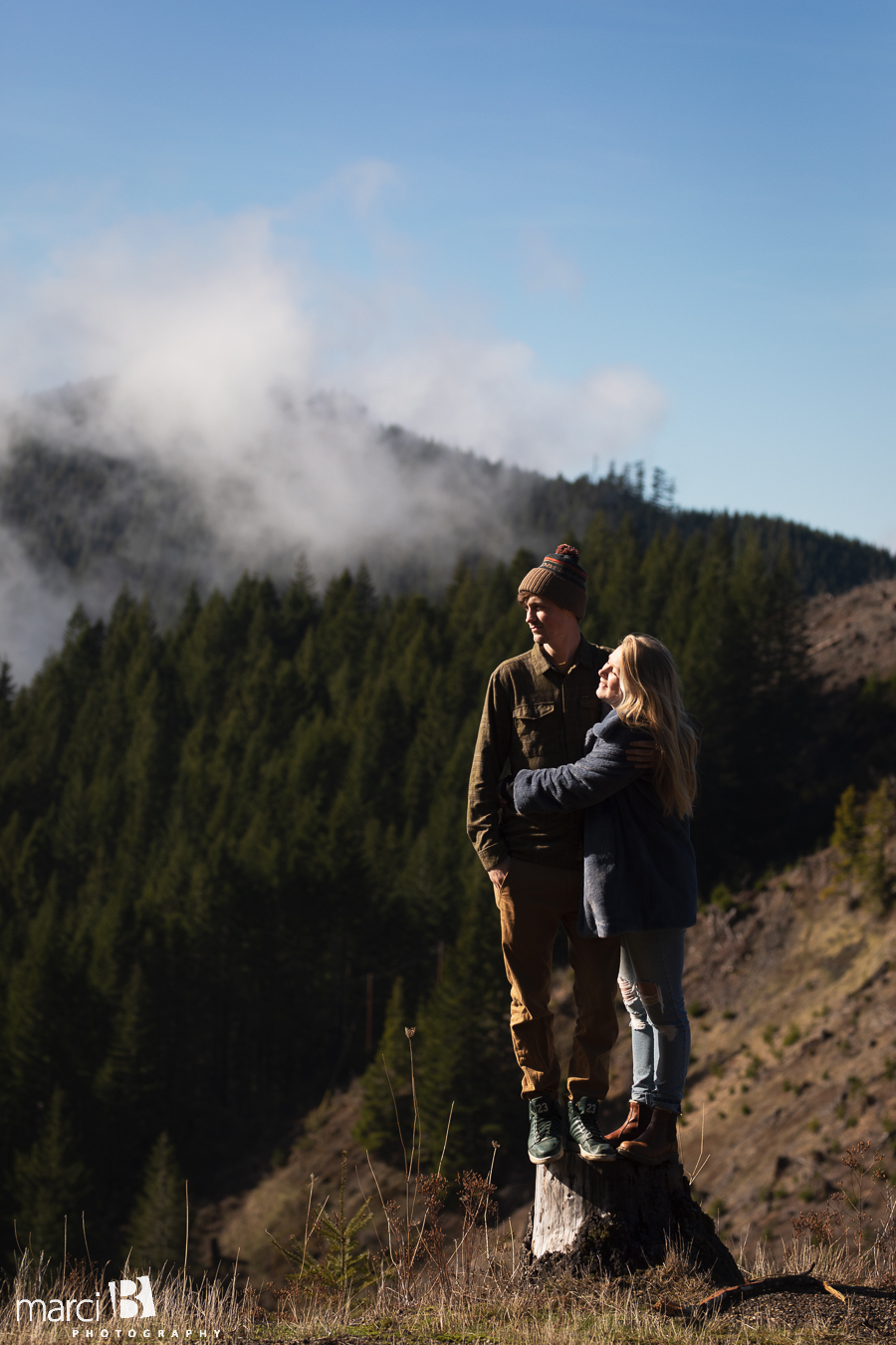 iconic pacific northwest couple standing on stump with green forest and clouds in background