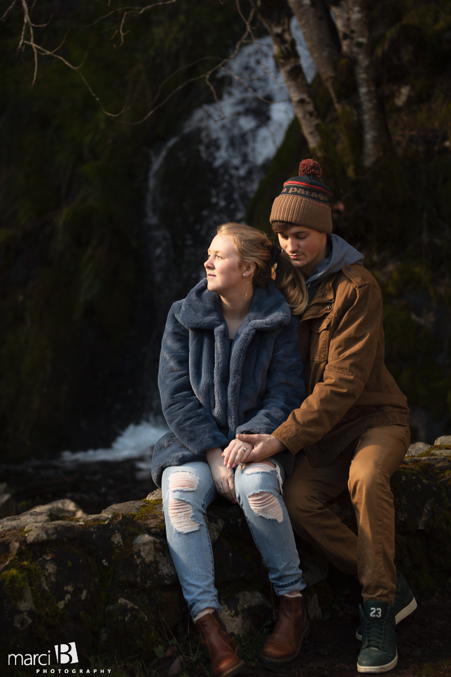 engaged couple sitting in front of Oregon waterfall